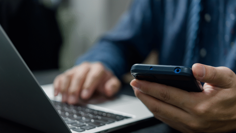 Mobil i handen på person som jobbar med datorn